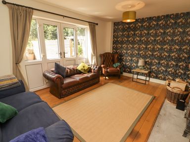 A living room with a brown leather sofa a blue sofa a brown armchair and a patterned wallpaper at Meadow Cottage in Llanarthney nr Llandeilo Carmarthenshire