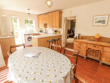 A kitchen with wooden cabinets a round dining table with a bee-patterned tablecloth and wooden chairs at Meadow Cottage in Llanarthney nr Llandeilo Carmarthenshire