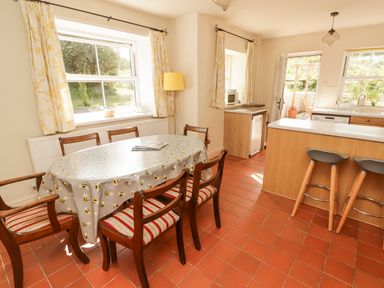 A kitchen dining area with a round table covered with a bee patterned cloth six wooden chairs two bar stools and windows with yellow floral curtains at Meadow Cottage in Llanarthney nr Llandeilo Carmarthenshire