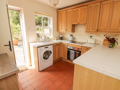 A kitchen with wooden cabinets a washing machine an oven and a window with a door leading outside at Meadow Cottage in Llanarthney nr Llandeilo Carmarthenshire