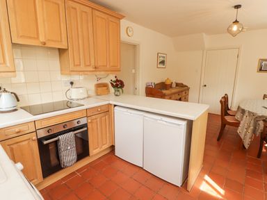 A kitchen with wooden cabinets two white appliances a dining table with chairs and a wooden sideboard at Meadow Cottage in Llanarthney nr Llandeilo Carmarthenshire
