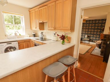 A kitchen with wooden cabinets a washing machine a sink an electric stove and two stools at Meadow Cottage in Llanarthney nr Llandeilo Carmarthenshire