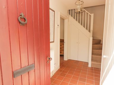 An entrance hallway with a red door terracotta tile floor a staircase with under stairs storage at Meadow Cottage in Llanarthney nr Llandeilo Carmarthenshire