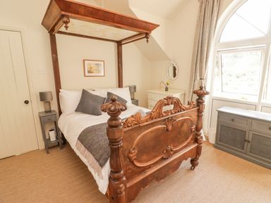 A bedroom with a wooden four-poster bed two bedside tables with lamps a dresser and a cabinet near a window at Meadow Cottage in Llanarthney nr Llandeilo Carmarthenshire