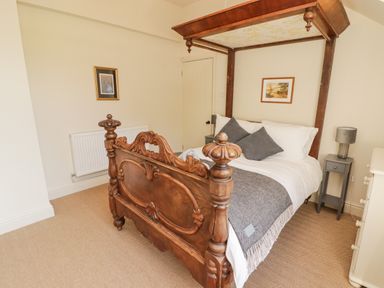 A bedroom with a wooden four-poster bed two gray pillows a gray blanket two side tables with lamps paintings on the walls at Meadow Cottage Llanarthney nr Llandeilo Carmarthenshire