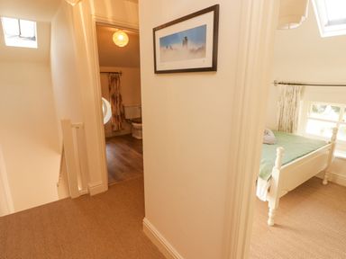 A hallway with a framed picture on the wall leading to a bathroom with a toilet and a bedroom with a bed at Meadow Cottage in Llanarthney nr Llandeilo Carmarthenshire