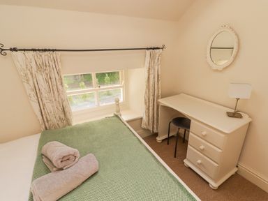 A bedroom with a bed covered by a green blanket and two towels a white desk with a chair a table lamp and a mirror on the wall at Meadow Cottage in Llanarthney nr Llandeilo Carmarthenshire
