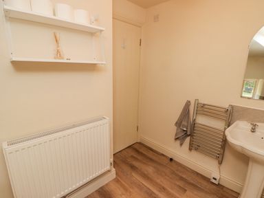 A bathroom with a door radiator shelf with containers towel rail and a sink at Meadow Cottage in Llanarthney nr Llandeilo Carmarthenshire