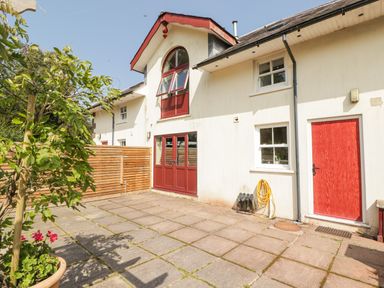 An outdoor patio area with tiled flooring a tree in a pot wooden fence and a building with red doors and windows at Meadow Cottage in Llanarthney nr Llandeilo Carmarthenshire