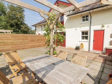 An outdoor patio area with a wooden table and chairs under a wooden pergola next to a white building with red doors at Meadow Cottage in Llanarthney nr Llandeilo Carmarthenshire