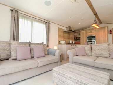 A living room with two sofas and an ottoman in front of a kitchen with wooden cabinets and appliances at Drake 11 in Cayton Bay