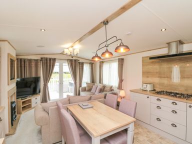 An open plan dining and living area with a dining table and chairs a sofa a TV and kitchen cabinets at Drake 11 in Cayton Bay