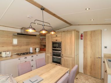 A kitchen with wooden cabinets a dining table with chairs and a ceiling light at Drake 11 in Cayton Bay