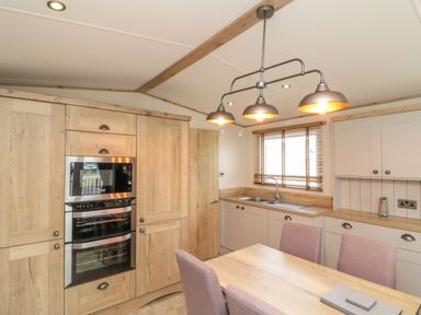 A kitchen with wooden cupboards a double oven a sink under a window and a wooden dining table with chairs at Drake 11 in Cayton Bay