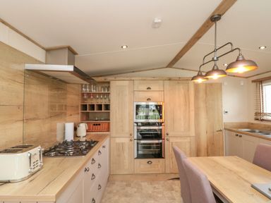 A kitchen with wooden cabinets a dining table with chairs a gas stove toaster kettle and oven at Drake 11 in Cayton Bay