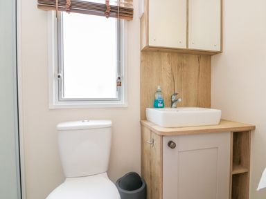 A bathroom with a toilet a sink with cabinet soap dispenser window and a trash bin at Drake 11 in Cayton Bay