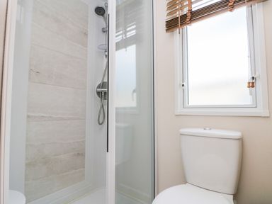 A bathroom with a shower enclosure a toilet and a window with blinds at Drake 11 in Cayton Bay