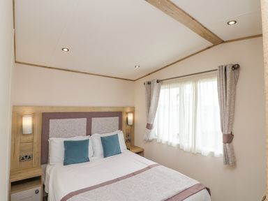 A bedroom with a double bed two blue cushions bedside tables and a window with curtains at Drake 11 in Cayton Bay