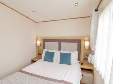 A bedroom with a bed against the wall two blue pillows on the bed bedside tables wall lamps and curtains at Drake 11 Cayton Bay