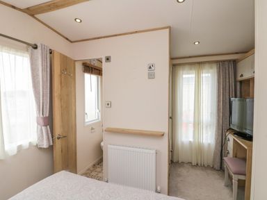 A bedroom with a bed a window a doorway to a bathroom a radiator and a TV on a desk at Drake 11 in Cayton Bay
