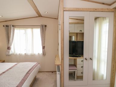 A bedroom with a bed near a window with curtains and a wardrobe with mirrored doors at Drake 11 in Cayton Bay