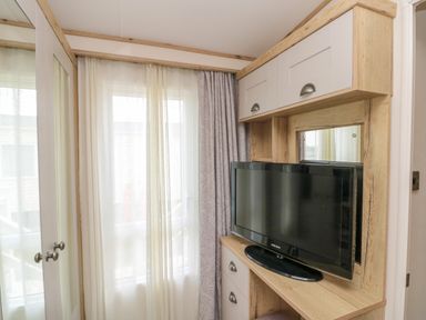 A bedroom corner with a wardrobe, a television on a wooden cabinet, and a window with curtains at Drake 11 in Cayton Bay