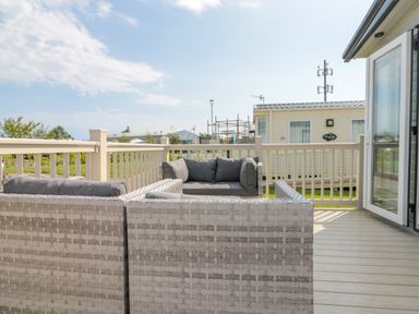 An outdoor patio area with wicker sofas with cushions and a railing with a view of other mobile homes at Drake 11 in Cayton Bay