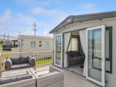 An outdoor seating area with wicker furniture and cushions next to a mobile home with glass doors open at Drake 11 in Cayton Bay