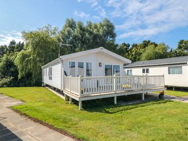 A white mobile home with a porch and railing on a grassy lot with trees in the background at 28 Finch in Cayton Bay