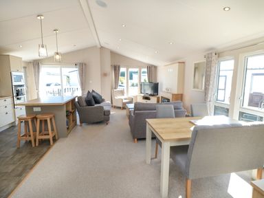 An open plan living room and kitchen with sofas dining table stools and a television at 28 Finch in Cayton Bay