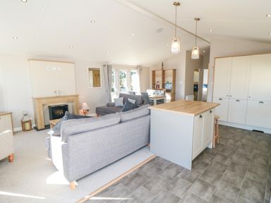 An open plan living room and kitchen with grey sofas a wooden fireplace a kitchen island and dining table at 28 Finch in Cayton Bay