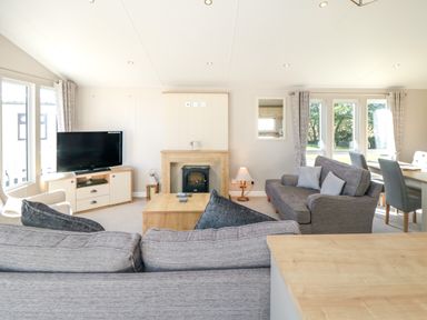 A living room with sofas a TV on a stand a coffee table and windows at 28 Finch in Cayton Bay