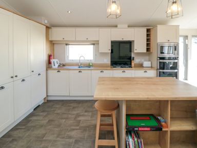 A kitchen with white cabinets a wooden island a stool a gas stove built in ovens and a window at 28 Finch in Cayton Bay