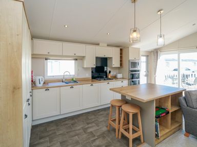 A kitchen with wooden countertop cabinets stove oven microwave two stools and sliding glass door at 28 Finch in Cayton Bay