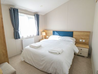 A bedroom with a bed with white linens two folded towels bedside tables and a window with patterned blue curtains at 28 Finch in Cayton Bay