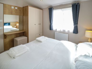 A bedroom with a bed, wardrobe, mirror, stool, window with curtains, and a lamp at 28 Finch in Cayton Bay