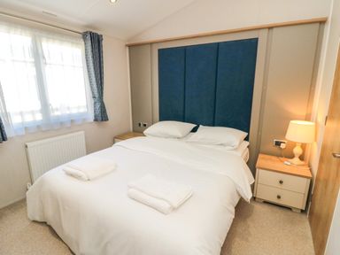 A bedroom with a bed white bedding two pillows folded towels bedside tables lamp and window with curtains at 28 Finch in Cayton Bay