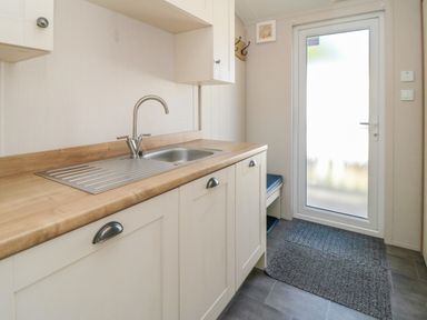 A kitchen area with a sink wooden countertop cabinets a frosted glass door and a floor mat at 28 Finch in Cayton Bay