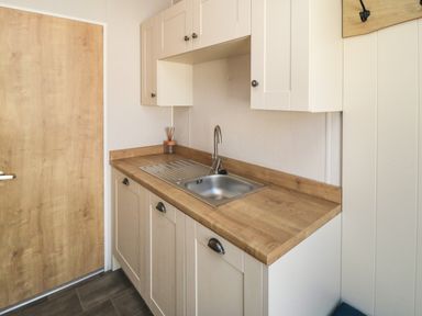 A kitchen with a wooden door white cabinets a stainless steel sink and a wooden countertop at 28 Finch in Cayton Bay