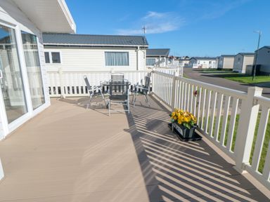 An outdoor deck with a table and chairs and a flower pot with yellow flowers at 28 Finch in Cayton Bay