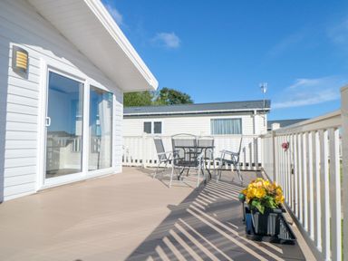 A deck with a glass table and four chairs a flower pot on the railing at 28 Finch in Cayton Bay