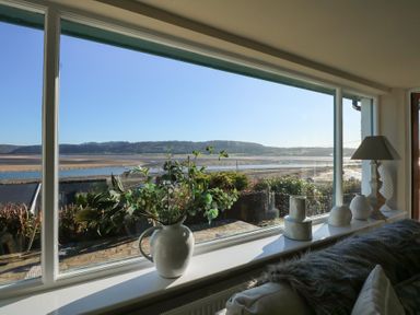 A windowsill with decorative vases and a lamp overlooking a beach and hills at Swn Y Wylan Red Wharf Bay near Benllech