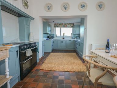 A kitchen with blue cabinets a black stove a wooden dining table with chairs and decorative plates on the wall at Swn Y Wylan Red Wharf Bay near Benllech