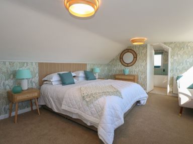 A bedroom with a large bed green pillows and lamps bedside tables a round mirror and an open door leading to a bathroom at Swn Y Wylan Red Wharf Bay near Benllech