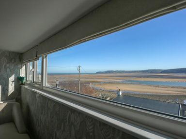 A room with a window overlooking a sandy beach and hills at Swn Y Wylan Red Wharf Bay near Benllech