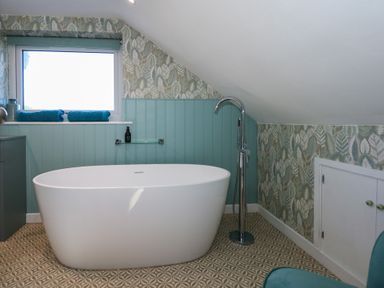 A bathroom with a freestanding bathtub under a window and patterned floor at Swn Y Wylan Red Wharf Bay near Benllech
