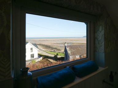 A window with two blue towels on the sill overlooking houses and a beach at Swn Y Wylan Red Wharf Bay near Benllech