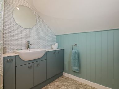 A bathroom with a sink and mirror above blue cabinets and a blue towel on a towel rack at Swn Y Wylan Red Wharf Bay near Benllech