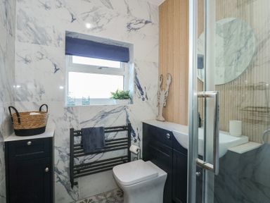 A bathroom with a toilet towel rack window and sink with cabinets at Swn Y Wylan Red Wharf Bay near Benllech
