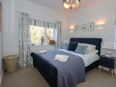A bedroom with a bed and pillows by a window with curtains at Swn Y Wylan in Red Wharf Bay near Benllech